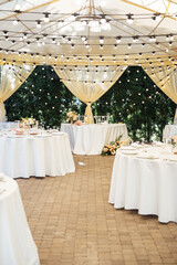 Evening decoration of a wedding party. Tables for guests with a garland and lamps