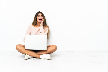 Young woman with a laptop sitting on the floor isolated on white background shouting with mouth wide open