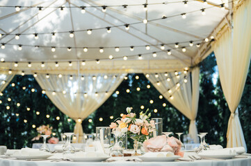 Evening decoration of a wedding party. Tables for guests with a garland and lamps