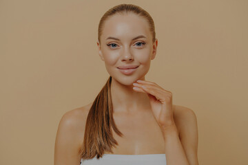 Beauty portrait of young well-groomed female touching soft pure skin after cosmetology procedure