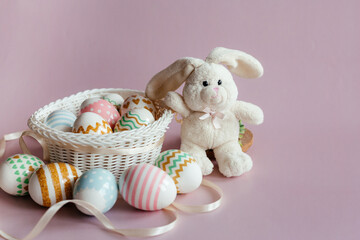 Fototapeta na wymiar Easter eggs in pastel colors with a pattern and a white toy rabbit in a basket