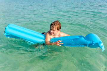 boy with red hair is enjoying  the air mattress at the crystal clear water