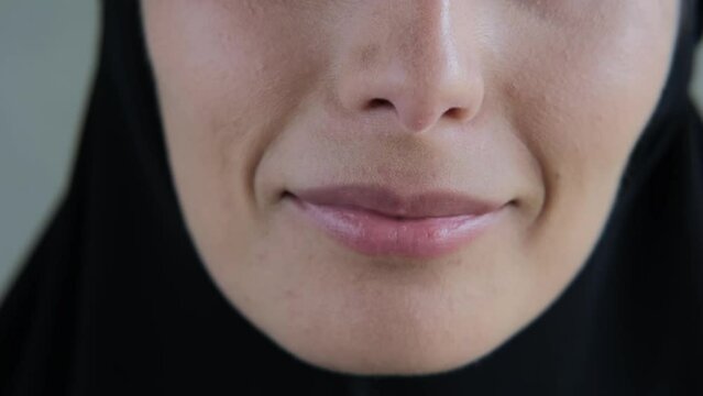 Close-up of the lips of a woman in a black hijab, a beautiful smile of a Muslim woman. The concept of goodness and peace in the Islamic world. Closeup of a woman's mouth.