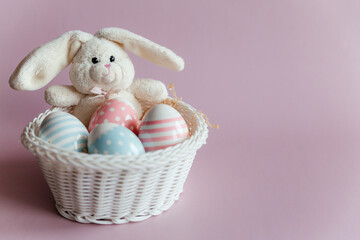 Fototapeta na wymiar Easter eggs in pastel colors with a pattern and a white toy rabbit in a basket