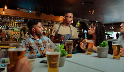 african american male waiter serving group of friends in restaurant