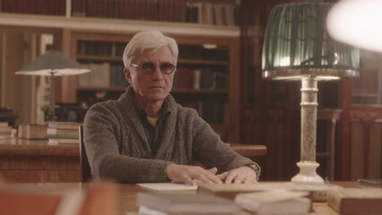 Medium slowmo of Caucasian senior man with disability reading Braille book at library