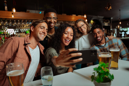 Group of young adult friends eating dinner at restaurant taking selfies