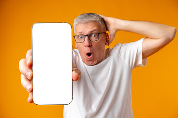Photo of senior surprised man point finger at smartphone over yellow background