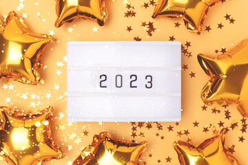 Lightbox with 2023 numbers on a gold colored background. Frame made of stars confetti and foil...