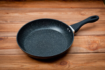 A round frying pan with a plastic handle is a utensil for frying food. Taken against the backdrop of a wooden table surface.
