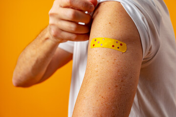 Man showing his shoulder with patch after covid 19 vaccine against yellow background