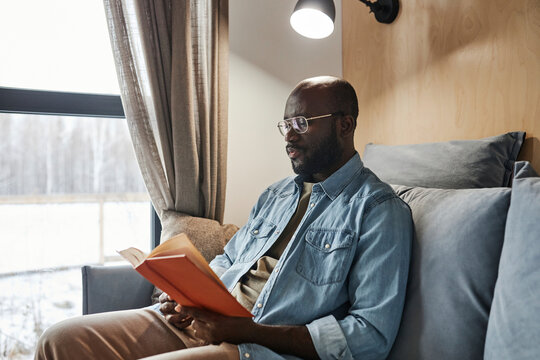 Young man reading novel on sofa at home