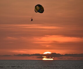 Silhouette of people parasailing in front of a setting sun 