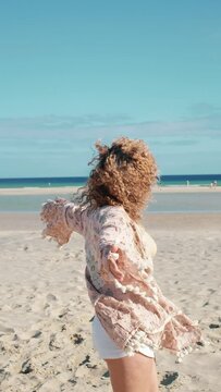 Happy young adult woman twirl at the beach enjoying sand and sun in tourist holiday travel vacation. Beautiful destination sandy lifestyle pretty female playing and smiling in outdoor leisure
