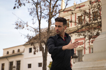Portrait of young Spanish man, wearing black shirt and pants, dancing flamenco in the street....