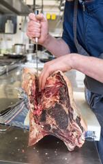 Gro&szlig;es Dry Aged Rippe Steak wird von einem Koch in der K&uuml;che mit einem Messer zerlegt und bearbeitet 