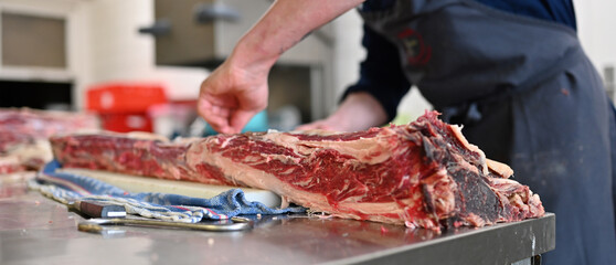 Großes Dry Aged Rippe Steak wird von einem Koch in der Küche mit einem Messer zerlegt und bearbeitet  - obrazy, fototapety, plakaty