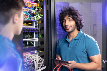 Technician holding tablet PC discussing with trainee in server room at industry