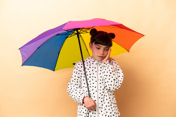 Little girl holding an umbrella isolated on beige background with headache