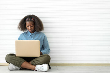 Fototapeta premium Portrait of smile black african american cute student little girl child sitting on floor using technology laptop computer typing on keyboard learn and study on white wall background