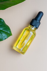 Glass bottle with cosmetic essential oil, fresh green leaves on beige background. Organic natural product. Flat lay, top view. Copy space.