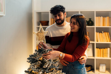 Happy couple decorating and putting star on Christmas tree at home
