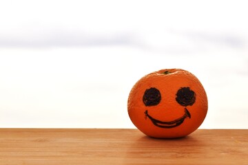 Orange painted with black happy eyes on a plank on a blurry white cloudy sky background.