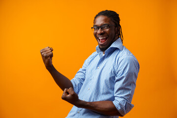 Portrait of overjoyed black man celebrating success with clenched fists against yellow background