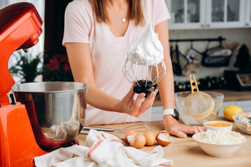 Young woman cooking meringue in the kitchen of her home. Process of cooking meringue. Whipped egg...