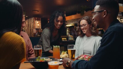 Diverse group of friends eating at restaurant while female waitress delivers food - Powered by Adobe