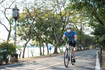 Asian young sport male wear face mask and ride bicycle in public park. 