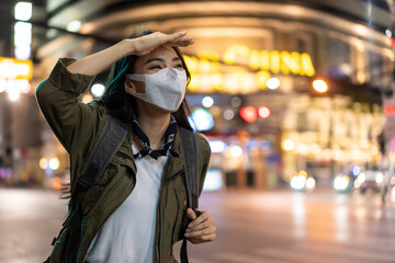 Asian young woman backpacker wear mask, wait for bus in city at night. 