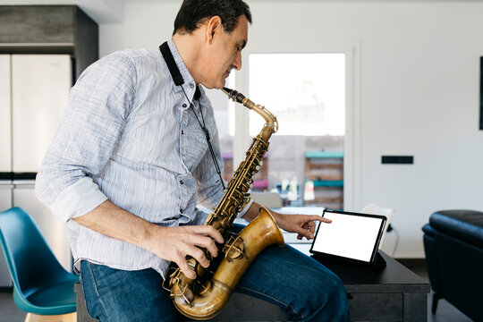 Musician with saxophone using tablet PC sitting on table at home+