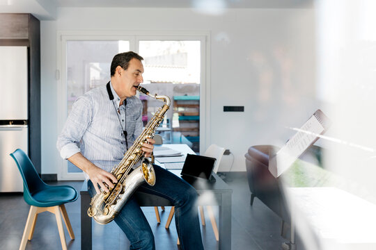 Saxophonist blowing saxophone sitting on table at home