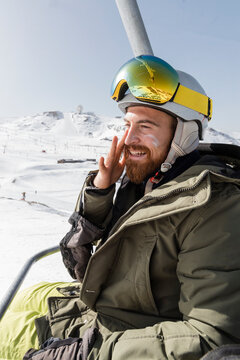 Smiling young man applying suntan lotion sitting on ski lift