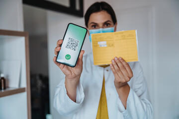 Female doctor showing vaccination certificate on smart phone at clinic