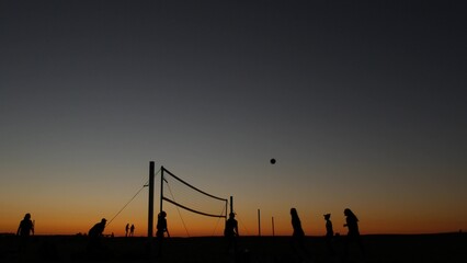 Fototapeta premium Volleyball net silhouette on beach sport court at sunset, people playing on California coast, USA. Sport field for volley ball game players by ocean shore. Twilight sky of Mission beach, San Diego.