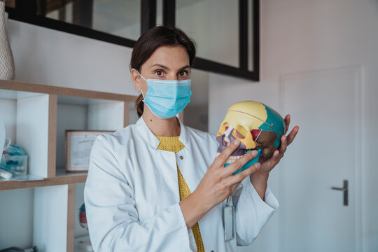 Doctor with protective face mask holding human skull in clinic