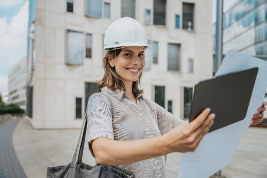 Smiling architect with blueprint and tablet PC at construction site