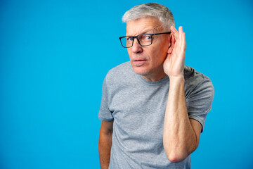 Middle age man over iblue background with hand over ear listening