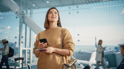 Airport Terminal: Happy Traveling Caucasian Woman Waiting at Flight Gates for Plane Boarding, Uses Mobile Smartphone, Checking Trip Destination on Internet. Smiling White Female on Vacation Trip