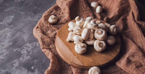 Fresh white champignons on a cutting board on a brown textile background. Kitchen, cooking, recipes. Mushrooms, ingredient. banner. Gray background