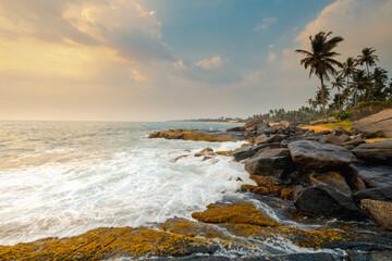 Foamy waves on the rocks and stones at the ocean coast under a beautiful sunset sky with clouds on Sri Lanka island.