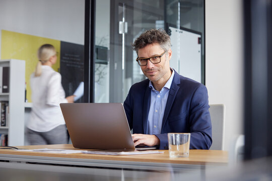 Businessman Wearing Eyeglasses Working On Laptop At Desk In Office