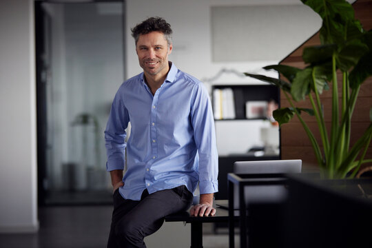 Smiling businessman with hand in pocket sitting on desk in office