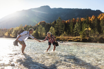 Austria, Alps, couple on a hiking trip wading in a brook