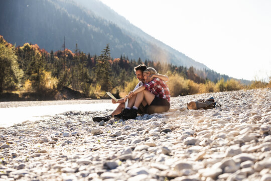 Austria, Alps, couple on a hiking trip having a break at a brook reading map