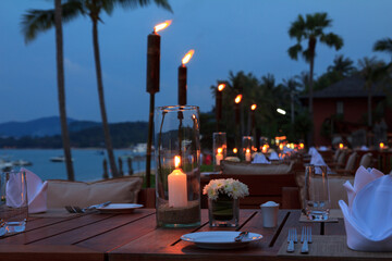 Outdoor restaurant romantic table dinner setting with candles and torches on tropical island beach at sunset