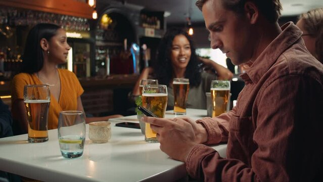 Caucasian male texting on cellular device while out for drinks with friends