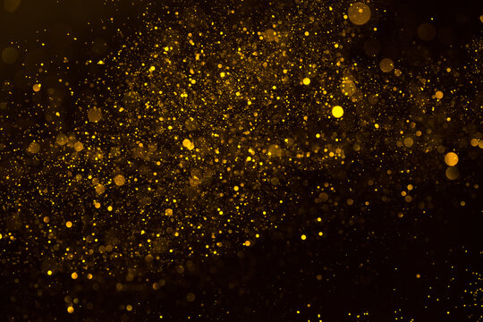 Abstract background of sparkling shiny golden glitter particles bokeh on black